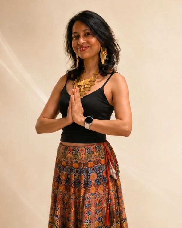 Subarna, standing with her hands together in namaste, in a black top and a hand-printed skirt.